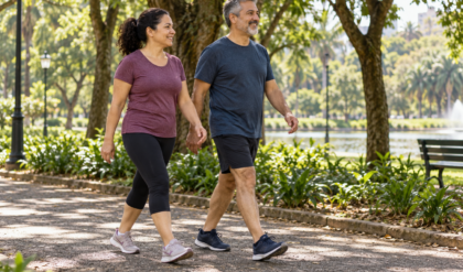 Dois adultos caminhando tranquilamente por uma pista plana e arborizada de parque.